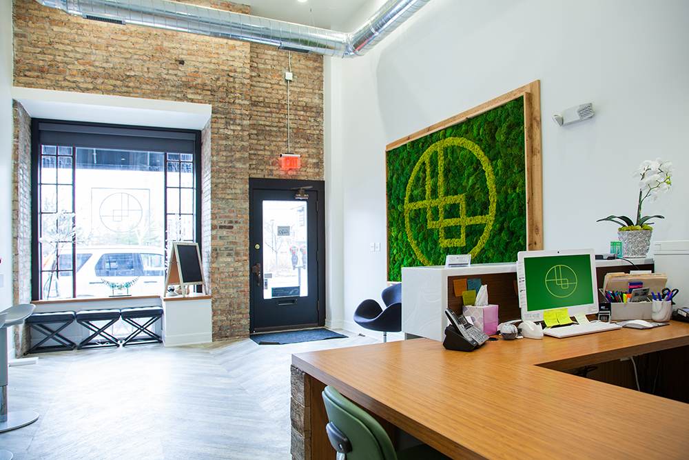 The Oak Park office: exposed brick, a moss wall in the shape of the Braces Boutique logo, and a wood reception desk.